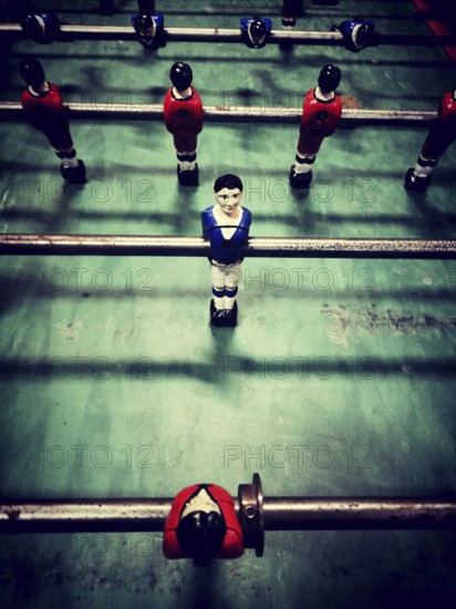 A lively table football game features diverse player figures in red, blue, and black, positioned on a green playing surface. Players compete for victory in a friendly match