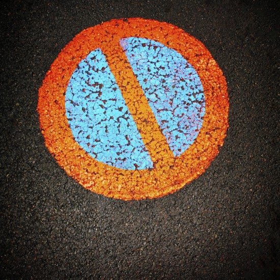 A vibrant no parking symbol is prominently displayed on a black asphalt surface, featuring a blue circle intersected by an orange diagonal line, creating a striking visual contrast