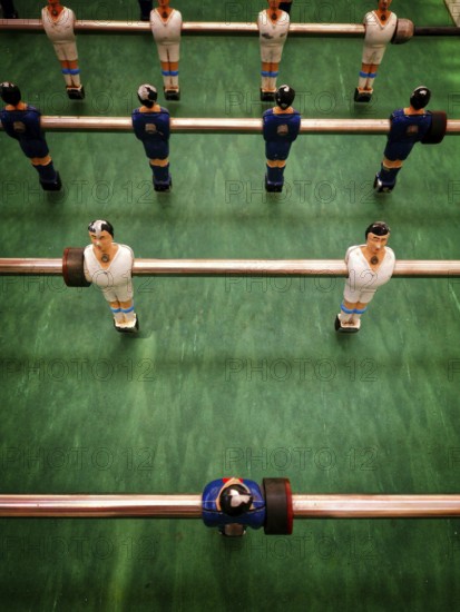 Players are set in a vintage table football game, ready for action. The colorful figures are positioned strategically, indicating an ongoing match among friends. Excitement fills the atmosphere
