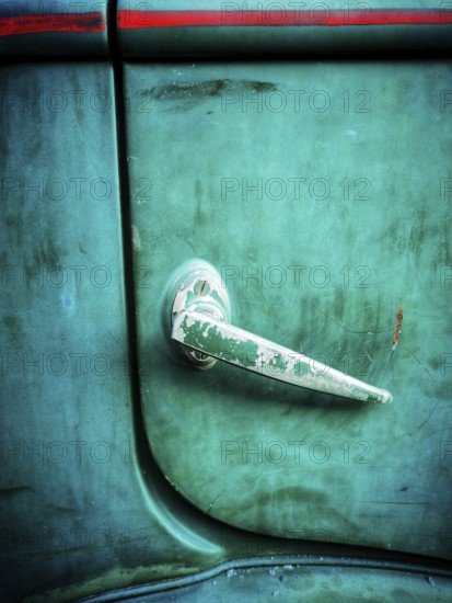 A close-up view of a vintage car door handle featuring a weathered surface and vibrant green paint. This detail showcases the charm of classic automobiles found outdoors