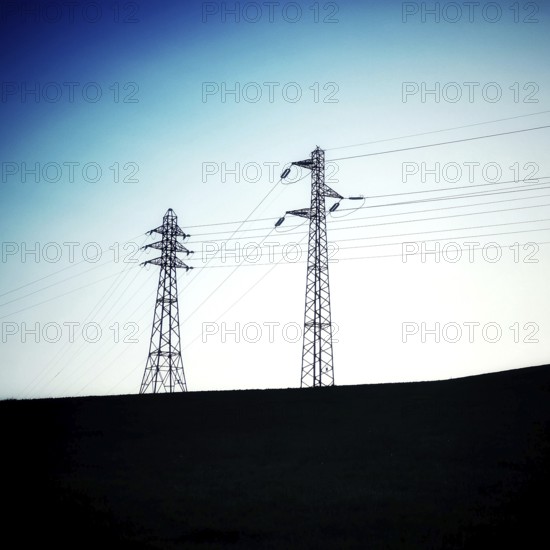 Two power towers reach upwards, silhouetted against a transitioning twilight sky. The horizon is gently rolling, creating a peaceful atmosphere during dusk