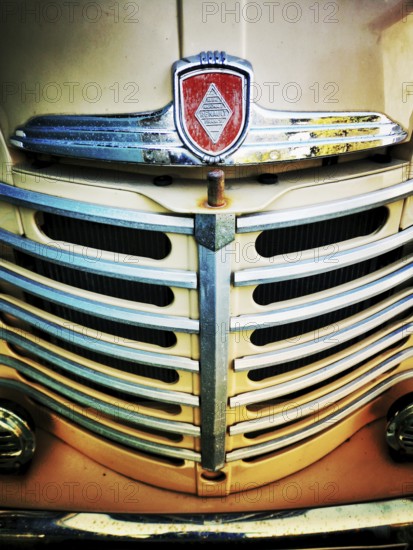 The front grille of a vintage truck features intricate chrome detailing with a prominent emblem. The weathered appearance reflects years of use and automotive design history