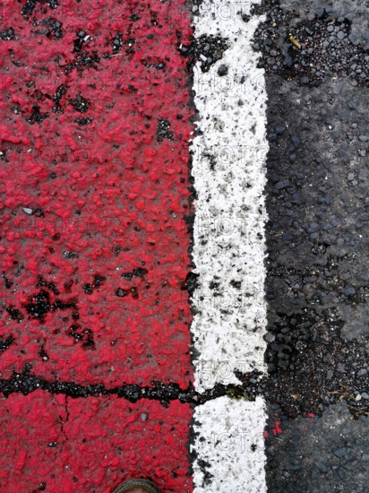 Bright red and white lines mark the asphalt surface, showcasing a clear division. A shoe is positioned close to the lines, adding perspective and detail to the scene