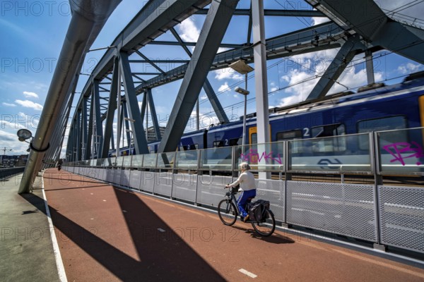 Cycle and pedestrian bridge Snelbinder Brug, over the river Waal near Nijmegen, was added to the existing railway bridge, fast cycle path connection from the city centre of Nijmegen and the new housing estates in the Waalsprong district, Netherlands