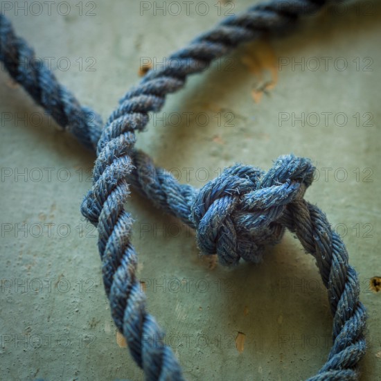 A close-up view reveals an intricately tied blue rope knot resting on a textured surface, highlighting the detailed craftsmanship involved in knot-making