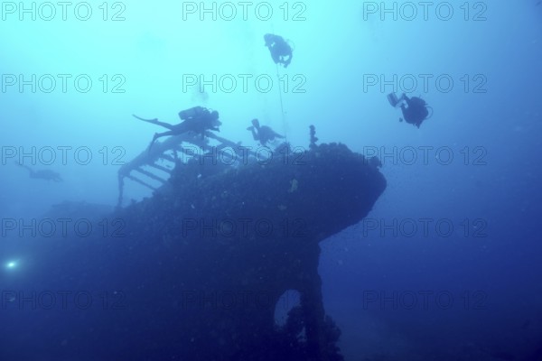 Divers circle the silhouette of an overgrown shipwreck in the blue water. Dive site wreck Le Grecq, Giens peninsula, Mediterranean Sea, Provence Alpes Côte d'Azur, France