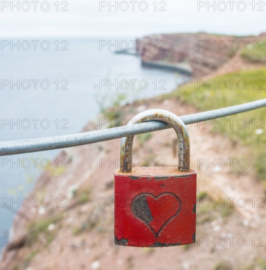 Red padlock with engraved heart symbol on a wire rope in front of the steep coast, red cliff of Heligoland, in the background the Lange Anna, view of the sea, love lock, rusty and romantic, Heligoland, Schleswig-Holstein, North Sea, Germany