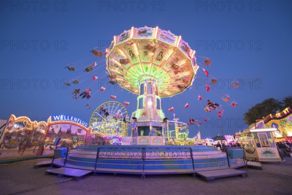 A chain carousel with lights turns at a fairground at dusk, chain carousel, spring festival, Cannstatter Wellenflug, illuminated, blue hour, Cannstatter Wasen, Bad Cannstatt, Stuttgart, Baden-Württemberg, Germany