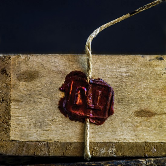 A wooden box is secured with twine, featuring a deep red wax seal that signifies authenticity and quality. The warm tones highlight traditional craftsmanship and care in presentation