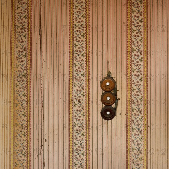 Intricate floral designs and charming stripes decorate the walls of an old building, while three circular buttons of old switch