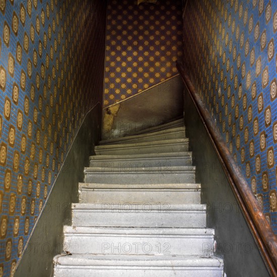 Staircase features worn steps and a dark atmosphere, going down to a lower level. The walls are adorned with patterned wallpaper, suggesting historical charm