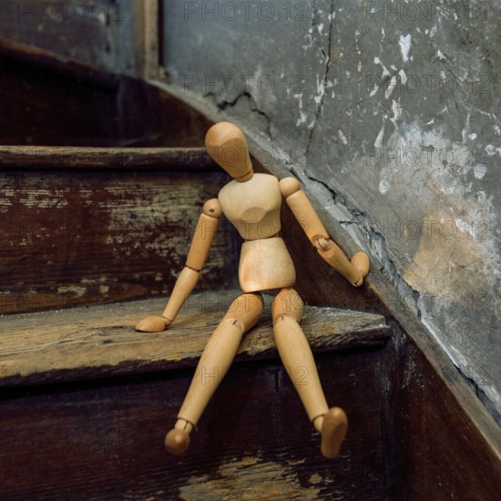 A wooden mannequin is seated casually on a weathered staircase, surrounded by rustic decor and peeling plaster. The scene captures a blend of artistry and nostalgia in a unique interior space