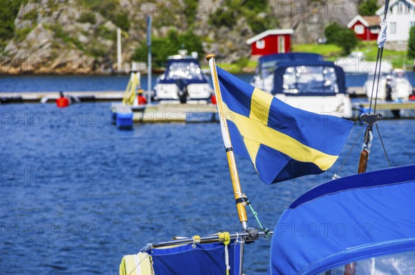 The Swedish flag flies at the stern of a boat in the marina of Henan on Orust, Bohuslän, Västra Götalands län, Sweden