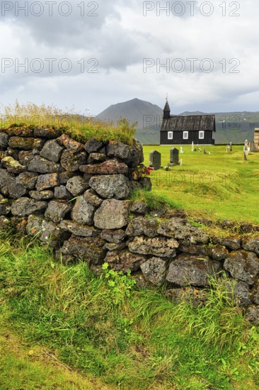 Traditional black church with cemetery, view through a stone wall to the wooden church Budakirkja, Búðir, Budir, Snaefellsnes Peninsula, Iceland