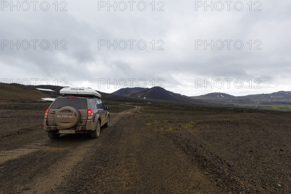 Off-road vehicle, SUV with roof tent driving on gravel track, barren volcanic landscape with snow fields, mountain peaks with rain clouds, Snaefellsjökull, Snæfellsnes peninsula, Snaefellsnes, West Iceland, Iceland