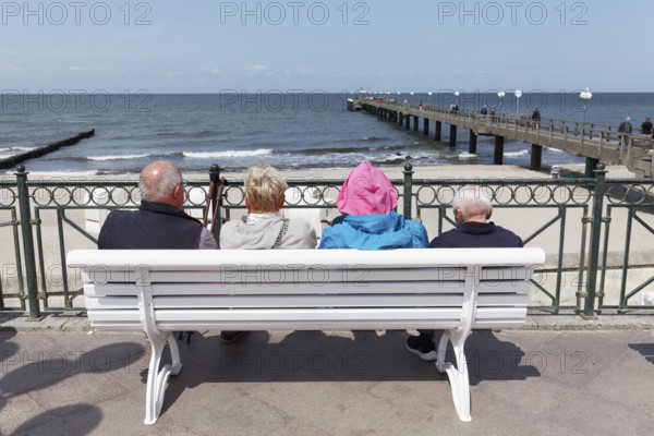Holidaymakers sitting on a bench on the beach promenade, one is wearing strikingly colourful clothes, Baltic resort Kühlungsborn, Baltic Sea, Mecklenburg-Western Pomerania, Germany