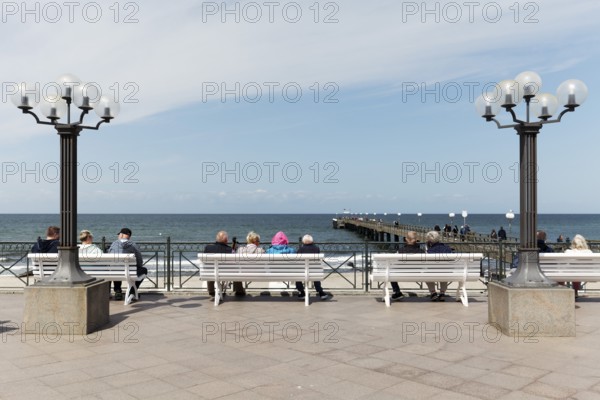 Holidaymakers sitting on benches on the beach promenade, one is wearing strikingly colourful clothes, Baltic resort Kühlungsborn, Baltic Sea, Mecklenburg-Western Pomerania, Germany