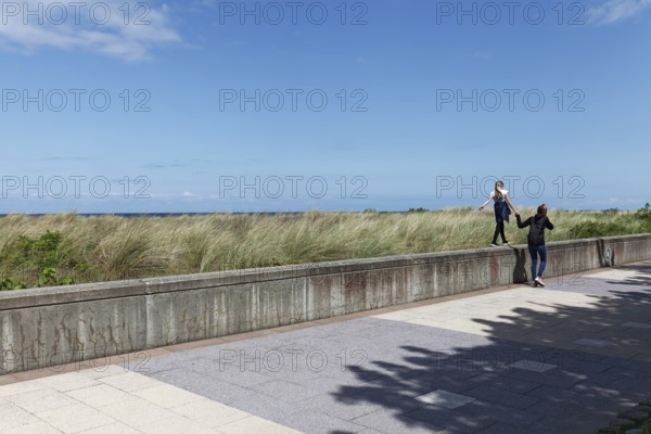Teenager leads little girl by the hand over a wall on the beach promenade, Baltic resort Kühlungsborn, Baltic Sea, Mecklenburg-Western Pomerania, Germany