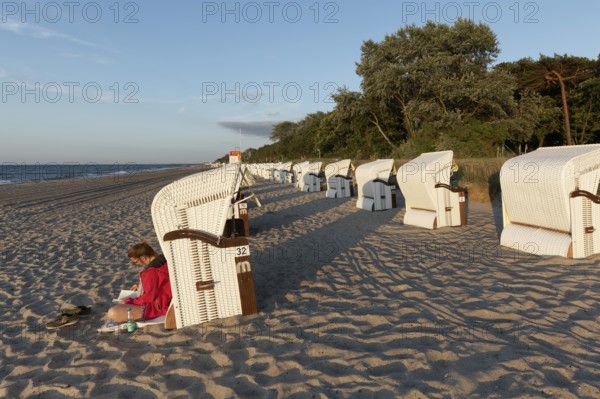 Woman reading a book in the evening sun, leaning against a beach chair, Baltic Sea near Kühlungsborn, Mecklenburg-Vorpommern, Germany
