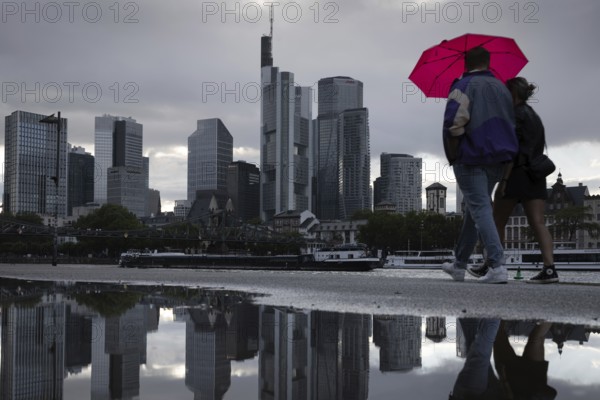 Two people walking in the rain under an umbrella in front of the Frankfurt bank skyline along the banks of the Main, Frankfurt am Main, Hesse, Germany