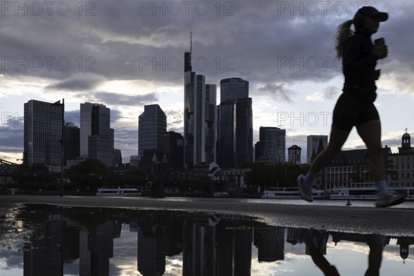 A jogger runs in the rain along the banks of the Main in front of the Frankfurt banking skyline, Frankfurt am Main, Hesse, Germany