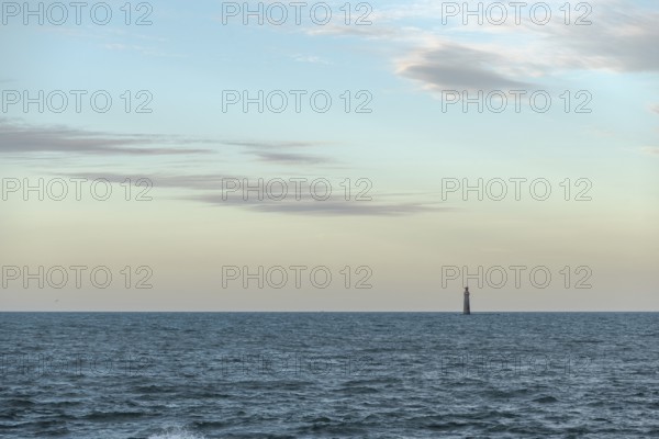 A lighthouse rises from the gentle waves of the ocean, surrounded by a tranquil seascape. Soft clouds drift over the sunset, creating a peaceful atmosphere. Les Sables d'Olonne, Vendee, France