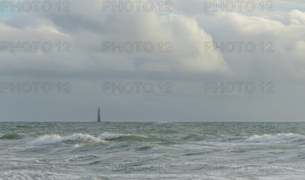 Waves crash against the shore while a lone lighthouse looms in the distance under a sky filled with dramatic clouds. The setting captures the calm yet powerful essence of the sea. Les Sables d'Olonne, Vendee, France