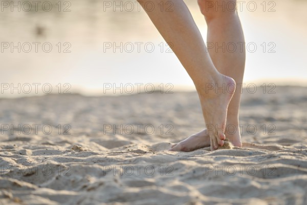 Soft sunlight illuminates a sandy beach as someone stands barefoot, feeling the warm sand beneath her feet. This peaceful moment captures the essence of summer relaxation by the water
