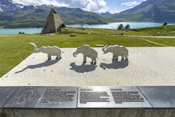 View from viewing platform to Mont-Cenis Pyramid Museum with stylised pyramid Museum in memory of Egypt campaigns of Emperor Napoleon Bonaparte and time in front of construction of reservoir, behind it Lac du Mont Cenis, in front on parapet small stylised figures of elephants Symbols for crossing of Alps Crossing of Alps by Hannibal, Mont Cenis Massif, Massif du Mont-Cenis, Graian Alps, Lanslebourg, Rhone-Alpes, France