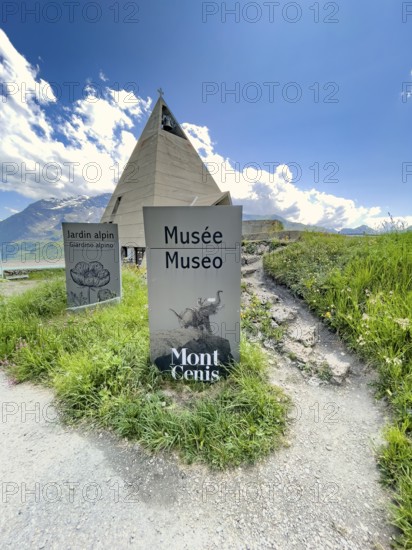 In front sign for Pyramid Museum Musée Museo Museum Mont Cenis, behind it Pyramid Museum with stylised pyramid in memory of Egyptian campaigns of Emperor Napoleon Bonaparte and time in front of construction of reservoir Lac du Mont Cenis, Mont Cenis Massif, Massif du Mont-Cenis, Graian Alps, Lanslebourg, Rhone-Alpes, France