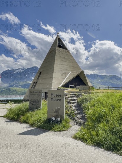 Mont-Cenis Pyramid Museum built in 1967 above the Lac du Mont Cenis in the form of a stylised pyramid as a museum to commemorate the Egyptian campaigns of Emperor Napoleon Bonaparte and the time in front of the construction of the reservoir, in the foreground a large free-standing Christian cross, Mont Cenis massif, Massif du Mont-Cenis, Graian Alps, Lanslebourg, Rhone-Alpes, France