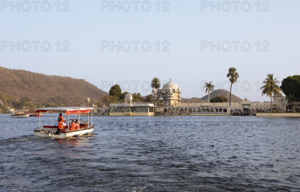 Excursion boat on Lake Pichola, behind Jagmandir Island Palace or Lake Garden Palace, Udaipur, Rajasthan, India