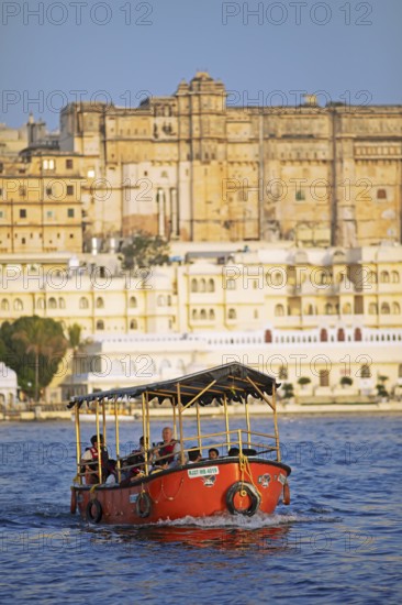 Electric excursion boat on Lake Pichola, behind the City Palace in the evening light, Udaipur, Rajasthan, India