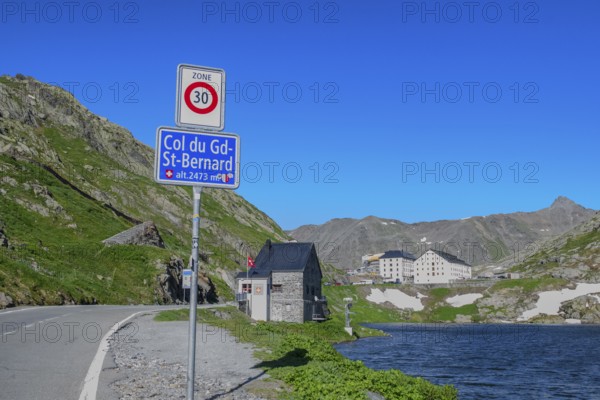 Traffic sign Speed limit sign 30 km/h below information Col du Gd-St.Bernard Grand Saint Bernard and altitude 2473 metres, behind it former border building at border crossing from Italy to Switzerland, in the background historic Auberge Herberge Hospice on top of the pass of Grand Saint Bernard, Saint-Rhémy-en-Bosses, Aosta Valley region, Italy