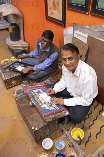 Miniature painters, 50 and 52 years old, painting pictures of the elephant and royal city palace in the studio, Udaipur, Rajasthan, India