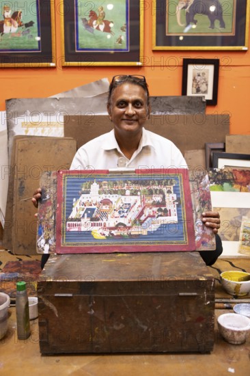 Miniature painter, 50 years old, shows a picture of the royal city palace in his studio, Udaipur, Rajasthan, India