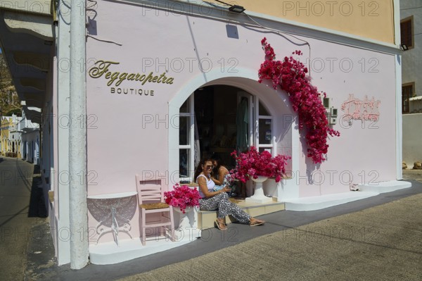 Pink boutique façade with blooming flowers, woman on the stairs, sunny and friendly atmosphere, Agia Marina, Leros, Dodecanese, Greek Islands, Greece