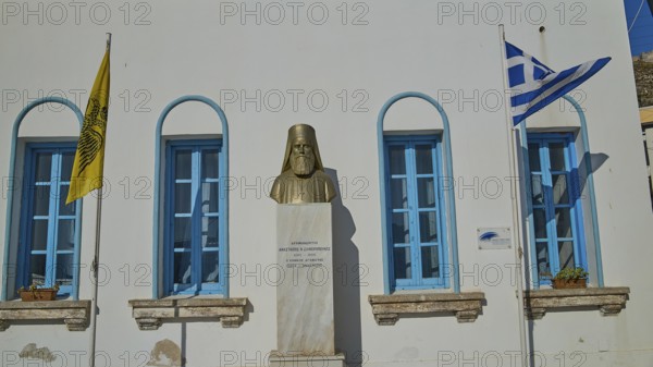 Archimandrite, Anastaios N. Zafeiropoulos, memorial bust between Greek and ecclesiastical flag in front of blue window front, Agia Marina, Leros, Dodecanese, Greek Islands, Greece