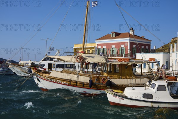 Wooden boats in the harbour with bright facades and Greek flags in calm waters, Agia Marina, Leros, Dodecanese, Greek Islands, Greece