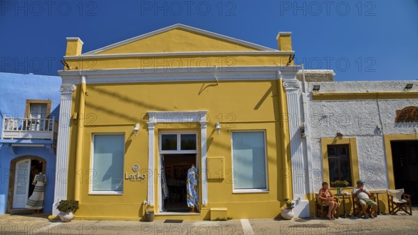 Yellow building with neoclassical facade, people in front of the door, clear blue sky, traditional atmosphere, Agia Marina, Leros, Dodecanese, Greek Islands, Greece