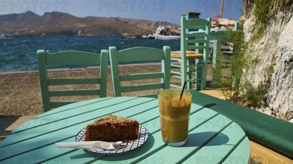 Turquoise-coloured table with drink and cake by the sea in sunny weather, relaxed atmosphere, Agia Marina, Leros, Dodecanese, Greek Islands, Greece