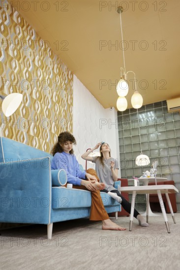 In a modern living room adorned with colorful wallpaper, two women are engaged in a fun skincare routine