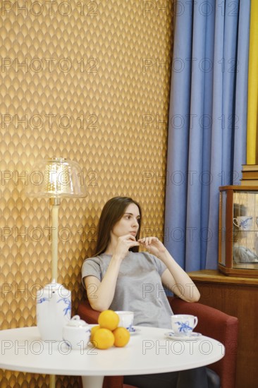 Young woman relaxing in a cozy living room with tea and fruit, surrounded by warm decor and soft lighting