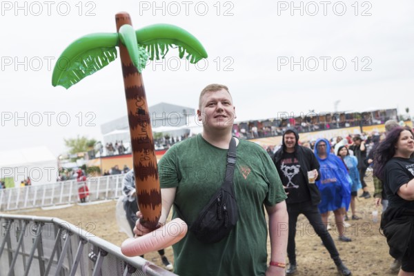 A festival visitor stands with an inflatable palm tree in the rain at the Highfield Festival on Sunday, Störmthaler See, 18/08/2024