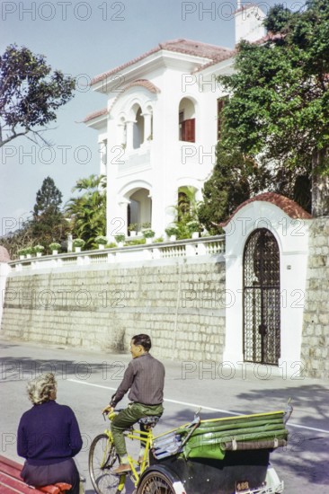 Tricycle rickshaw rider outside Portuguese colonial villa building, Avenida da Republica, Macau, Asia 1964