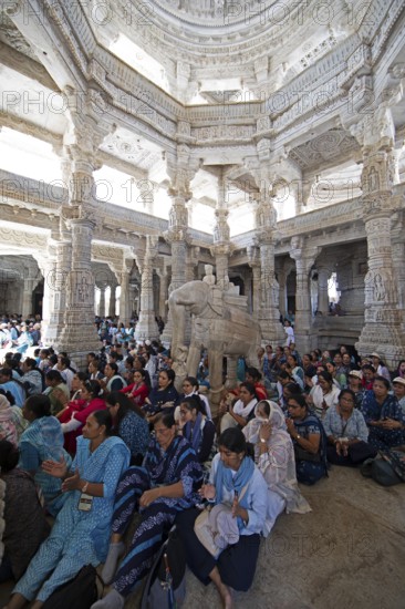 Indian woman pray between the white marble pillars around a marble elephant statue in the Adinath temple in Ranakpur, Jain temple, Rajasthan, India