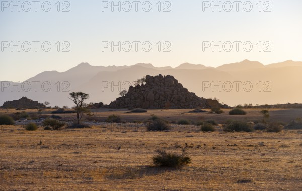 Desert landscape in the evening light at sunset, barren landscape with hills of stacked rocks, backlit, Brandberg in the background, Erongo, Damaraland, Namibia