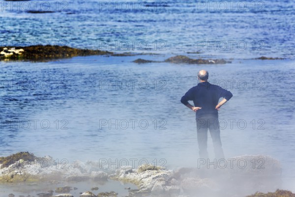 Hot spring flows into the sea, tourist on steaming rocky coast near Reykjanes, Súðavík, Ísafjarðardjúp fjord, Vestfirðir, Westfjords, Iceland