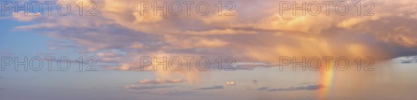 Background image for sky replacement, evening sky with illuminated clouds, rain shower and rainbow at sunset