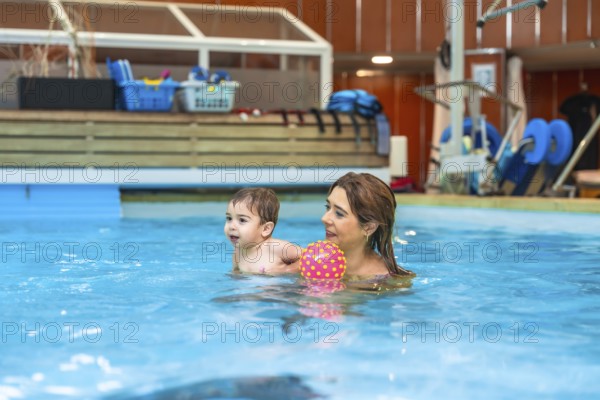 Mother and son having fun together playing with a colorful inflatable ball during a swimming lesson in an indoor pool